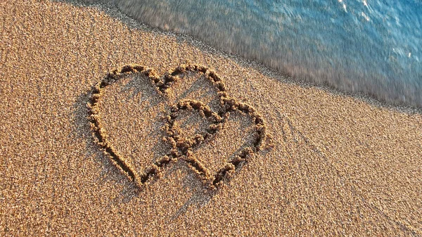 Two hearts drawn on brown sand of paradise beach — Stock fotografie