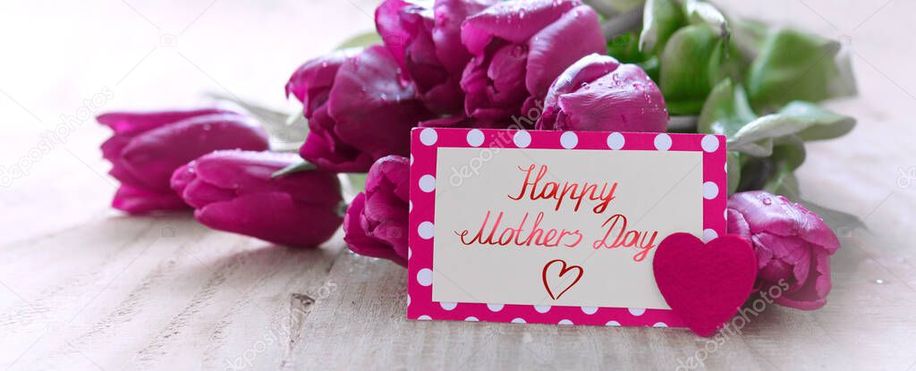 Happy Mothers Day card with purple tulips on wood background.