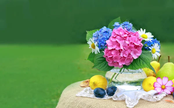 Барвистий букет квітів у скляній вазі та свіжих змішаних фруктах  . — стокове фото
