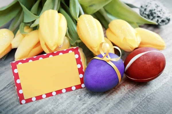 Easter background with colorful eggs and yellow tulips. — Stock Photo, Image