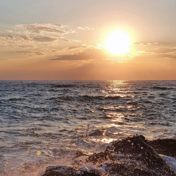 Deniz dalgalarının altında güneşli, renkli bir gün batımı.