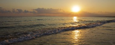 Bir dalga ve kum ile altın bir güneş doğuyor. Yunanistan beach.