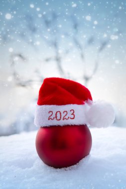 Beyaz karda kırmızı Noel Baba şapkası ve noel balosu. Yeni yıl 2023 arkaplanı.