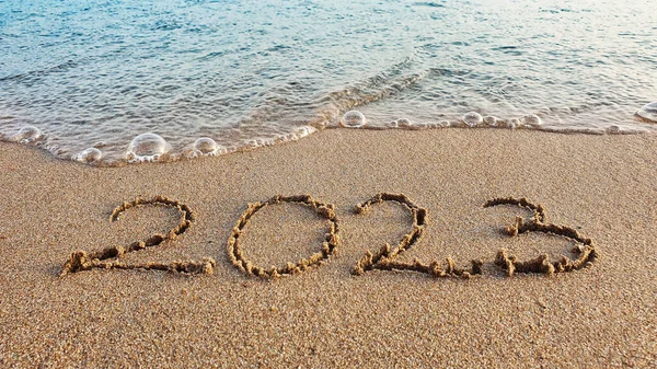Happy New Year 2023 text on the sea beach. Handwritten inscription 2023 on beautiful golden sand beach