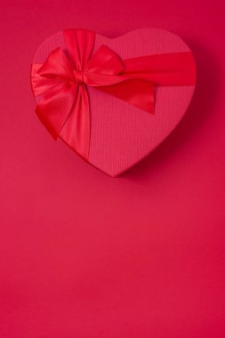 Kırmızı arka planda sevgililer günü hediyesi - kırmızı kalp kutusu ve yay