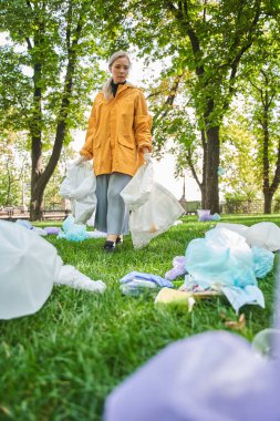 Parkta elinde çöp poşeti olan ve çöp toplayan bir kadın.