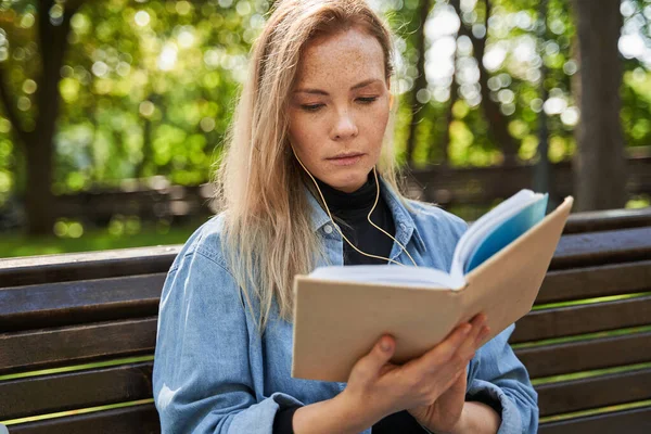 Young woman is reading interesting book in the park