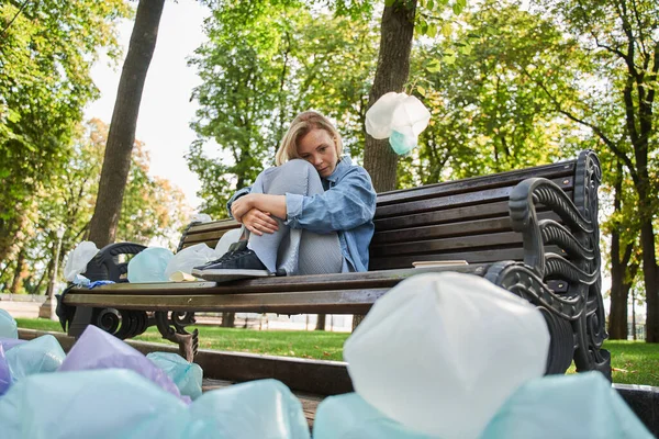 Woman sitting at the bench and being afraid of the great amount of rubbish around her