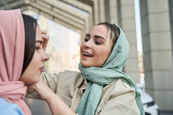 Mujer islámica alisa el cabello y el pañuelo para la cabeza a su mejor amigo mientras está de pie —  Fotos de Stock