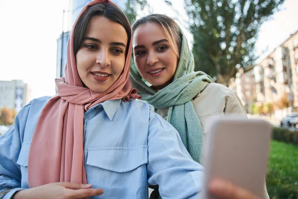 Muszlim lányok kötődnek egymáshoz, és együtt fotóznak a modern okostelefonon. — Stock Fotó