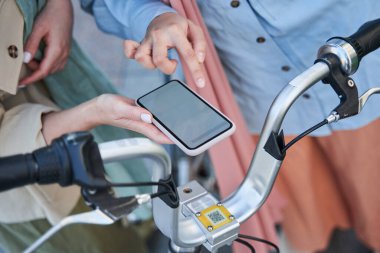 İki kadın, şehirde yürümek için bisiklet kilidini açmak için akıllı telefon kullanıyor.