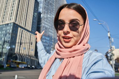 Başörtüsü takan kadın aletine bakıyor ve yüksek mimariyi işaret ediyor.