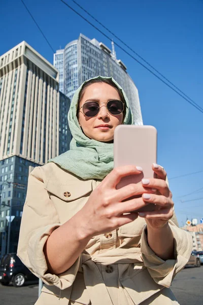 Muszlim lány szelfi okostelefon magas épületek a háttérben — Stock Fotó