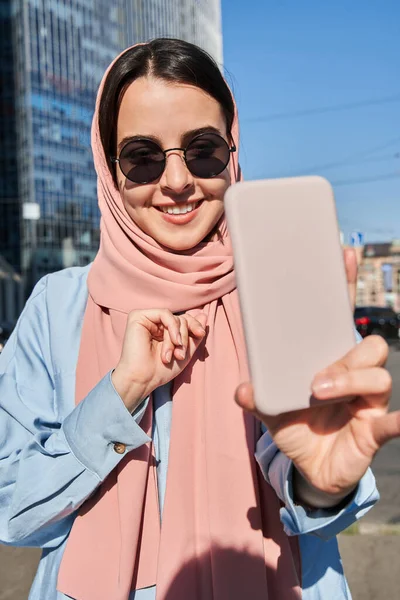 Iszlám hölgy visel fejkendő és napszemüveg, hogy szelfi okostelefon — Stock Fotó