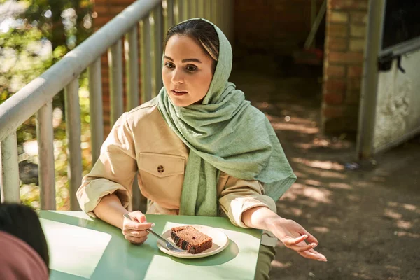 Mujer islámica vistiendo gestos de abaya mientras habla algo a su mejor amiga —  Fotos de Stock
