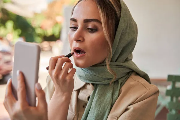 Egy nő nézi a tükörképét az okostelefonon, és különleges ceruzával festi az ajkait. — Stock Fotó