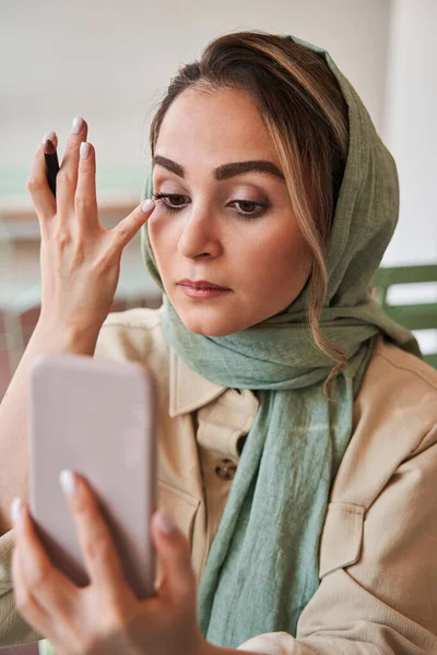 Az iszlám nő fejkendőt visel, befesti a szempilláit, és a cellájában lévő szelfi kamerát nézi. — Stock Fotó