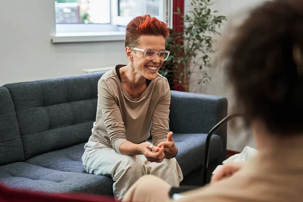 Woman laughing out loud while sitting at sofa and talking with her doctor during therapy