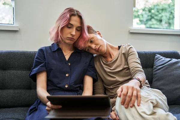 Lesbian couple sitting on the couch and looking at the tablet screen while listening — Stock Photo, Image