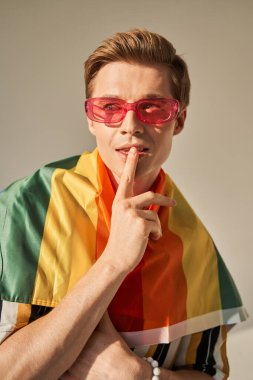 LGBT gökkuşağı bayraklı bir adam omuzlarında sessizce jest yapıyor ve şehvetli bakışlar atıyor.