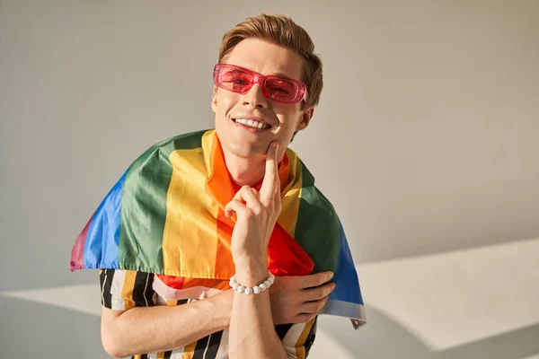 Gay hombre vistiendo lgbt orgullo bandera y rosa gafas en su cara, tocando mejilla y mirando — Foto de Stock