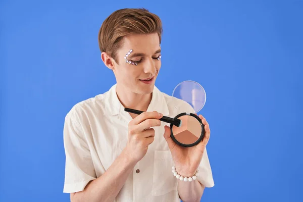 Excéntrico bisexual hombre sosteniendo maquillaje paleta y mostrando con el pincel en el tono — Foto de Stock