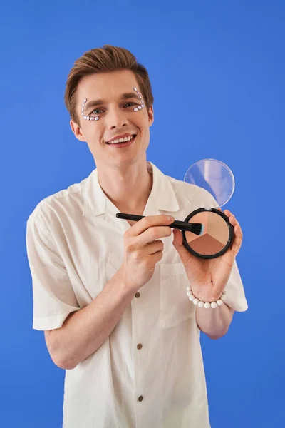 Queer Mann mit Strass im Gesicht zeigt Palette zum Konturieren in die Kamera — Stockfoto