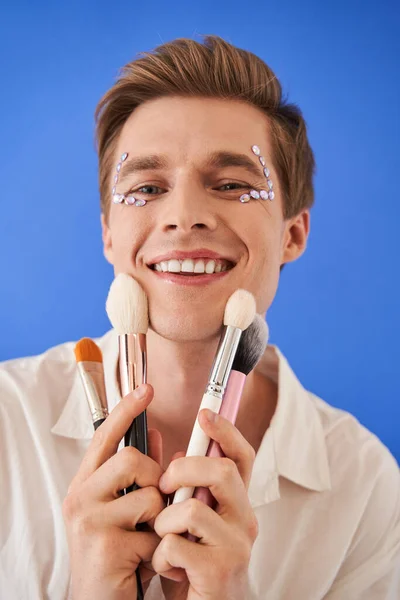 Muž s kreativním make-upem drží tvář kartáče a usmívá se do kamery — Stock fotografie