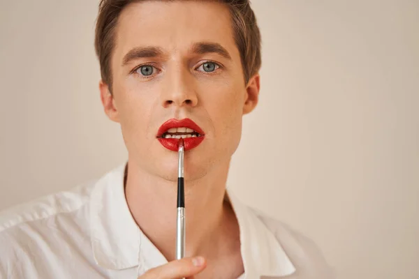 Modelo masculino fluido de género con lápiz labial rojo mirando con ojos penetrantes a la cámara — Foto de Stock