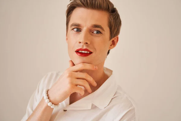Bisexual maquillaje artista con lápiz labial rojo mirando hacia otro lado mientras posando —  Fotos de Stock