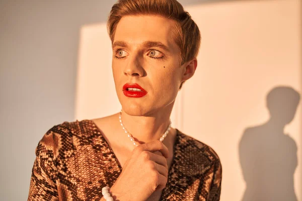 Hombre andrógino con joyas y maquillaje mirando hacia otro lado con expresión seria — Foto de Stock