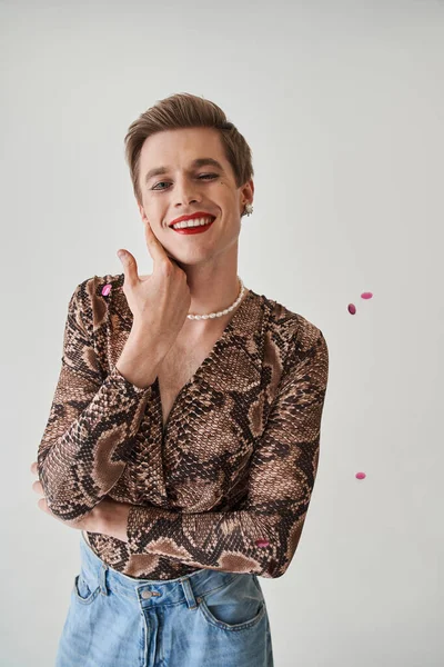 Zufriedener femininer Kerl, der seine Tussi berührt und zahm lächelt, während er im Studio posiert — Stockfoto