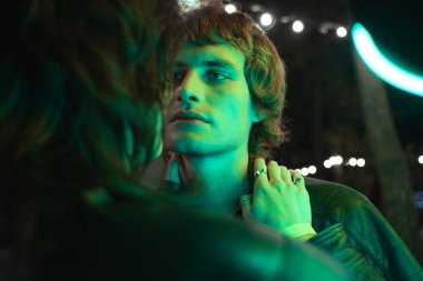 Neon ışıkları altında romantik bir buluşma sırasında bir kadın güzel erkeğine elleriyle dokunuyor.