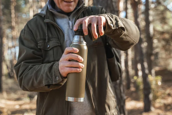 Senior man preparing to pouring warm tea from the thermos with kind smile — Stock Photo, Image