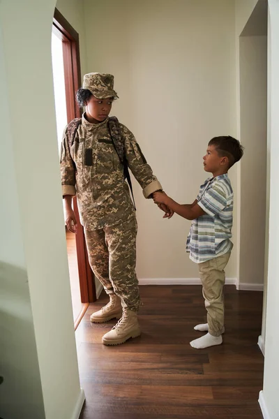 Niño cogido de la mano de su madre soldado mientras la despide al ejército en el pasillo — Foto de Stock