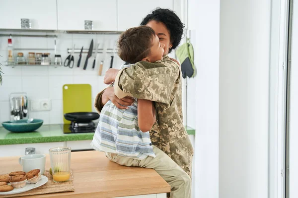 Чорна мати обіймає свого маленького сина на кухні — стокове фото