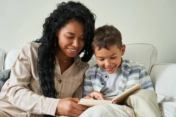 Preto mãe leitura livro com ela filho no sofá — Fotografia de Stock