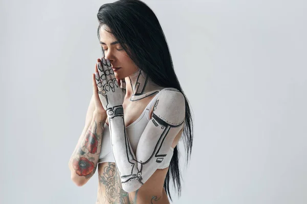 Tatuerad flicka med cyborg kropp konst på handen poserar med slutna ögon och bön gest — Stockfoto