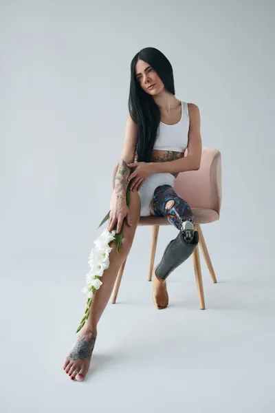 Женщина с искусственной ногой сидит на стуле, позируя в студии с цветами — стоковое фото