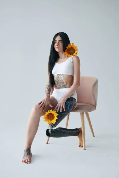 Женщина с искусственной ногой сидит на стуле, позируя в студии с подсолнухами — стоковое фото