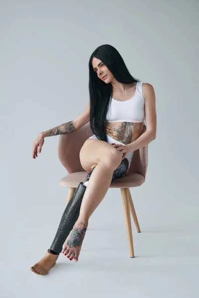 Женщина с механической протезной ногой и татуировками на теле позирует в студии — стоковое фото