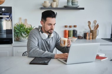 Kulaklık takan adam evde çalışırken sabah kahvesini içiyor.