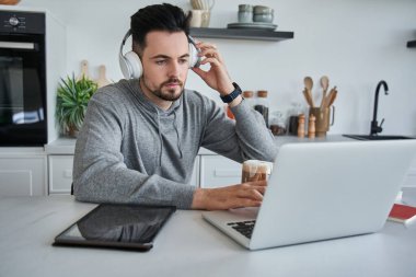 Kulaklıklı yakışıklı genç adam evde defter üzerinde çalışıyor.