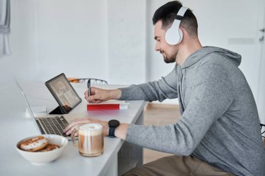 Kafkasyalı bir adam iş arkadaşlarıyla görüntülü konuşma yaparken not alıyor.