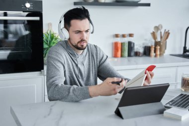 Adam dizüstü bilgisayar kullanarak internet ya da internet eğitimi izlerken deftere notlar yazıyor