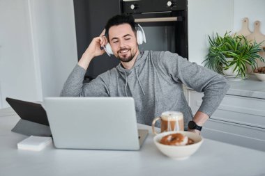 Kulaklık takan bir adam çalışırken dizüstü bilgisayara bakıp gülümsedi.