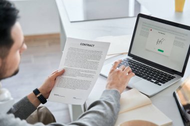 Adam kontratı tutuyor ve dizüstü bilgisayardaki elektronik şarkıya bakıyor.