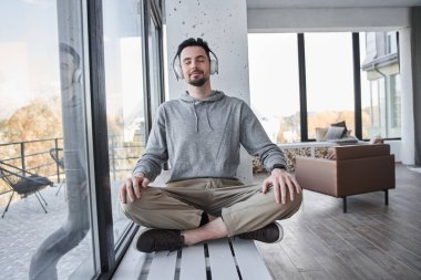 Pencere kenarında oturmuş, meditasyon yaparken yoga yapan bir adam.