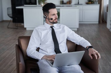 Kulaklık takan, resmi kıyafetler giyen, koltukta oturan ve başka tarafa bakan bir adam.