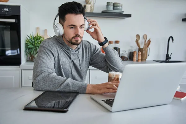 Kulaklıklı yakışıklı genç adam evde defter üzerinde çalışıyor.